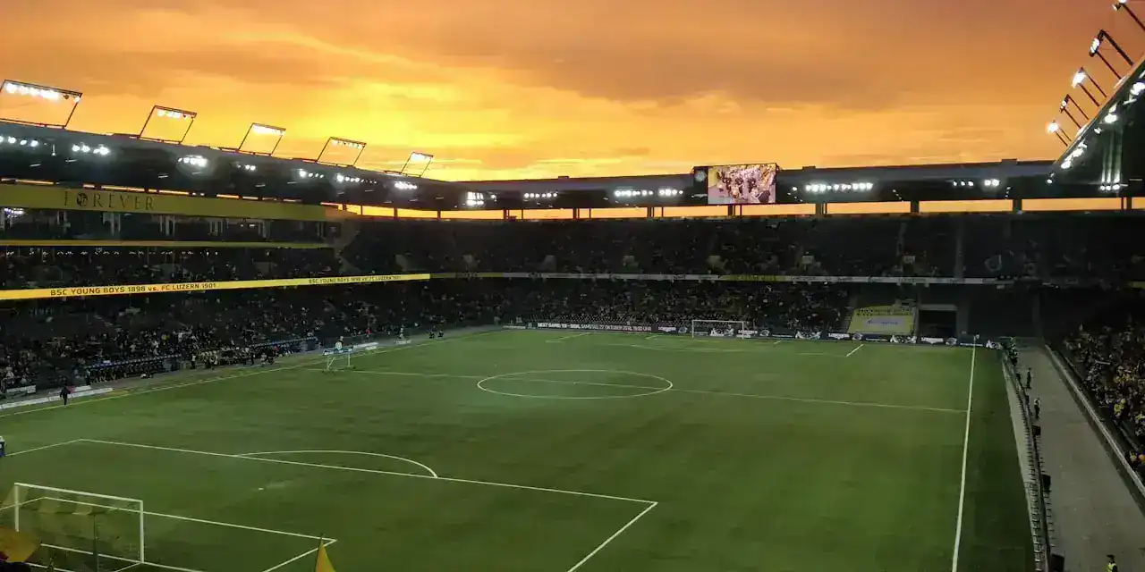 Bancadas iluminadas de um grande estádio de futebol ao entardecer